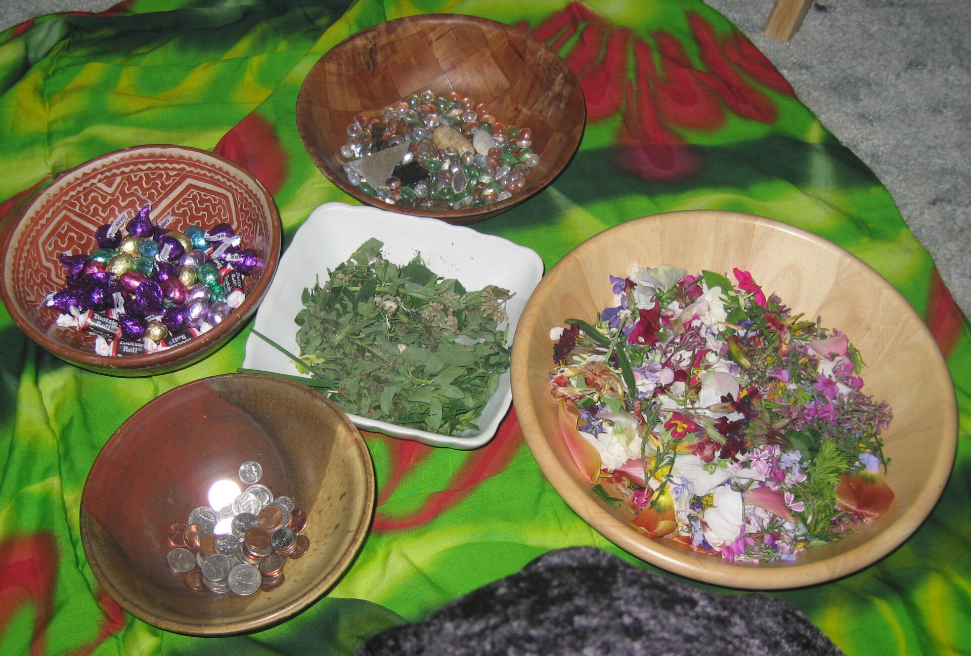 Five assorted bowls, each containing a symbol of abundance: chocolate for love, herbs for health, coins for prosperity, flowers for beauty, stones for stability