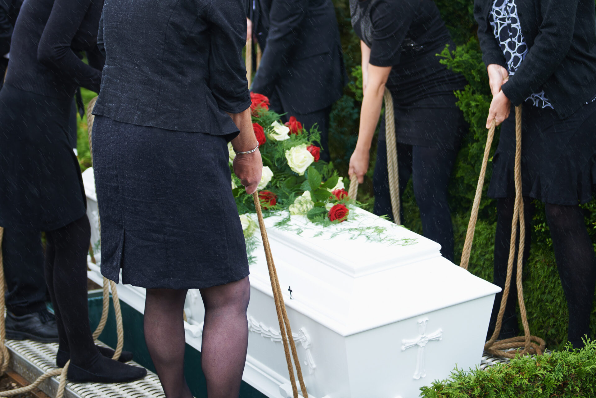 Six people in black lower a casket into a grave