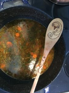 A wooden spoon with an owl design rests on the edge of a pot of soup. The spoon is part of a spiritual ritual.