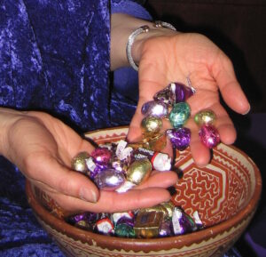 Two hands scoop colorfully wrapped chocolates from a pretty bowl