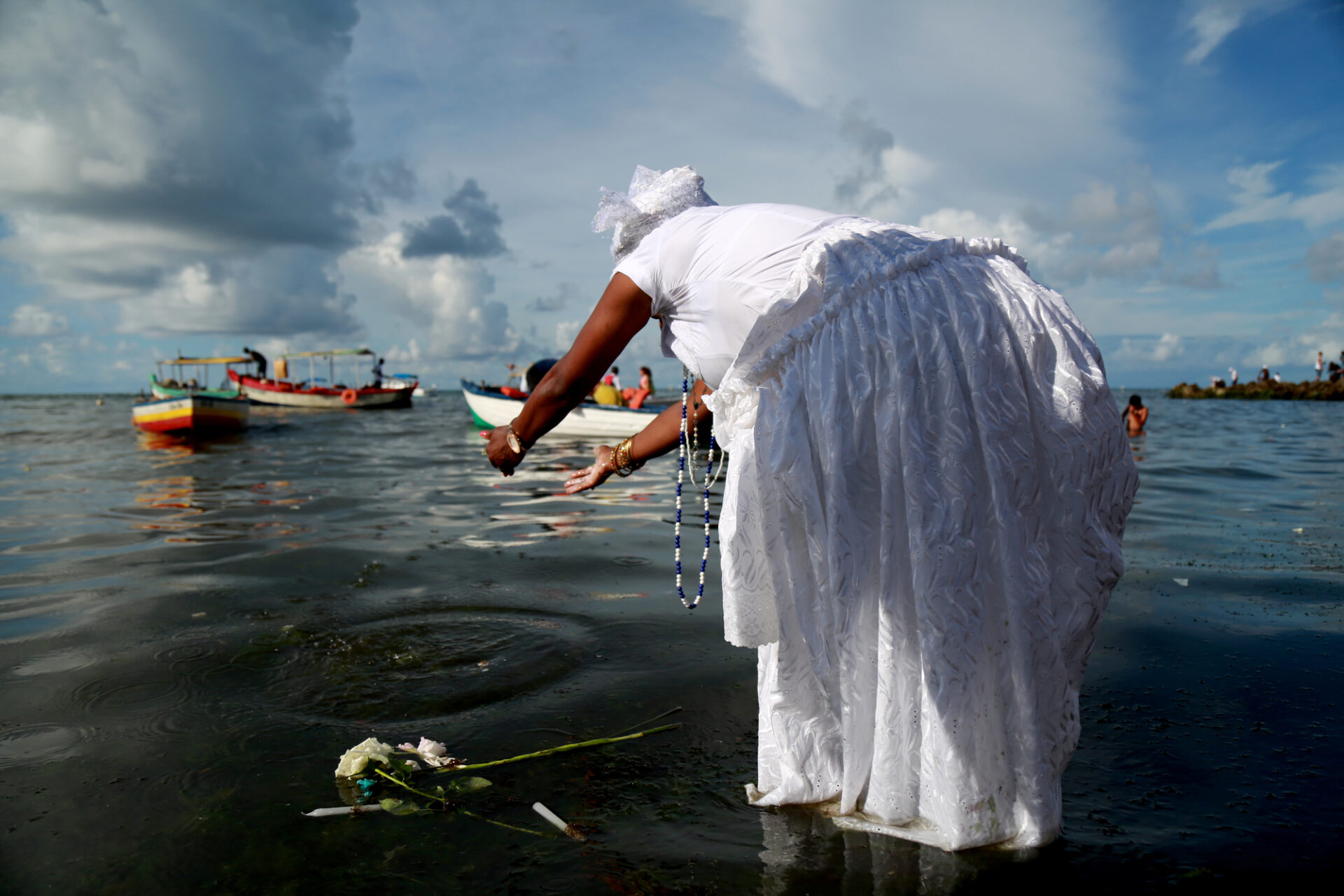 Woman in white gown drops flowers on the ocean to honor Yemaya